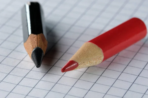 古い小さな使用された鋭利な赤と黒の木製のスレートの鉛筆は チェッカー紙シート クローズアップに横たわっています — ストック写真