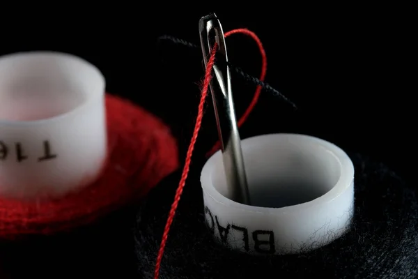 赤と黒の糸のスプールと黒の背景に糸で挿入された針クローズアップマクロ写真 — ストック写真