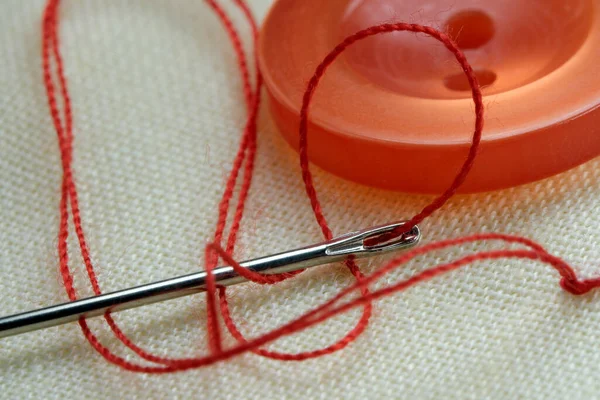 白いリネンの布の上に糸を挿入した針で赤いボタンを閉じるマクロ写真 — ストック写真