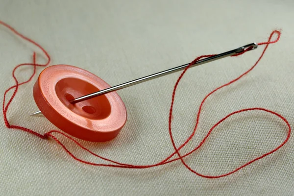 白いリネンの布の上に糸を挿入した針で赤いボタンを閉じるマクロ写真 — ストック写真