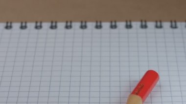Keskinleştirilmiş küçük bir kırmızı tahta kalem görünür ve açık kareli bir defter, video klip, yakın plan üzerinde durur.