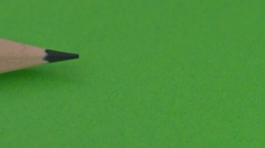 Solda basit bir tahta kalem görünür, sağdaki bir kalem tarafından engellenir, yeşil arkaplanda bir silgi, video klipsi, yakın plan