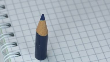 Keskinleştirilmiş küçük mavi, yeşil ve kırmızı kalemler açık kareli bir defterde görünür ve ayağa kalkar, yakın çekim, yavaş çekim, video klipte