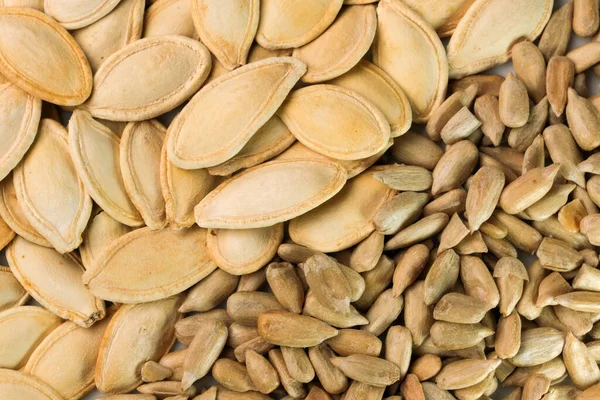 Kavrulmuş kabak çekirdekleri ve kavrulmuş ayçiçeği çekirdekleri arka planda dikey tam ekran görüntüsü.