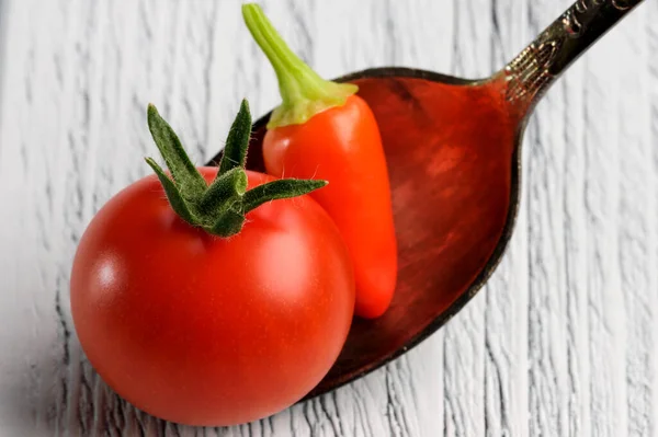 小さな赤い熟したトマトと赤唐辛子を小さじ1杯の軽い木製の背景のクローズアップ — ストック写真