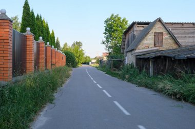 Yazın kırsal alanda, asfalt yol boyunca modern kır evleri ve çitler var.