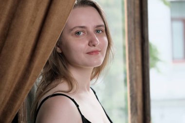 Portrait of a young attractive brown-haired girl at the open door to the balcony close-up