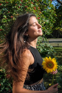 Young cute girl with long straight hair in a black crop top with a sunflower
