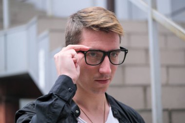Portrait of a young handsome guy in a black shirt with glasses close-up autumn street photography