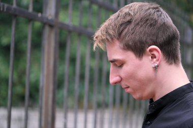 Portrait of a young handsome guy profile close-up against the background of a metal fence autumn street photography