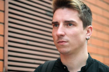 Portrait of a young handsome guy in a black shirt next to a brick wall autumn street photography