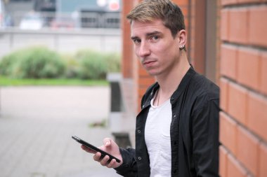 Portrait of a young handsome guy in a black shirt next to a brick wall autumn street photography