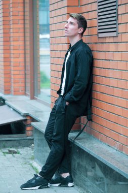 Portrait of a young handsome guy in a black shirt next to a brick wall autumn street photography