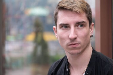 Portrait of a young handsome guy in a black shirt next to a shop window autumn street photography