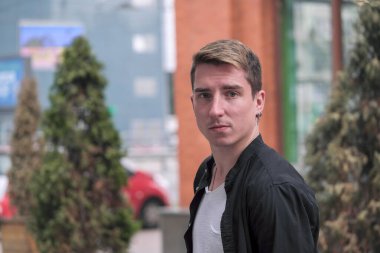 Portrait of a young handsome guy in a black shirt next to a brick wall autumn street photography