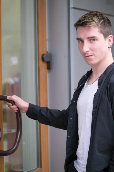 Portrait of a young handsome guy in a black shirt opens the door close-up autumn street photography