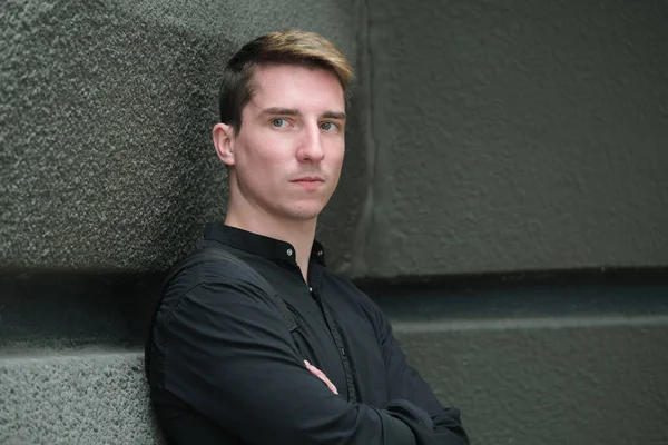 Portrait of a young handsome guy in a black shirt next to a brick wall autumn street photography