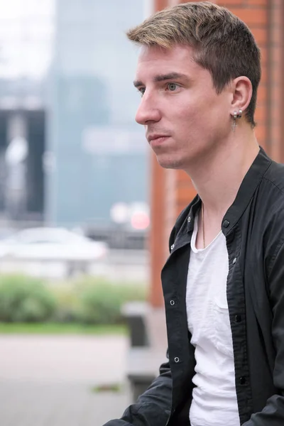 Portrait of a young handsome guy in a black shirt next to a brick wall autumn street photography