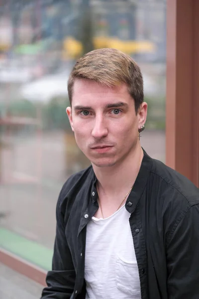 Portrait of a young handsome guy in a black shirt next to a shop window autumn street photography