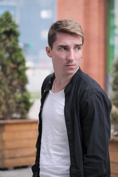 Portrait of a young handsome guy in a black shirt next to a brick wall autumn street photography