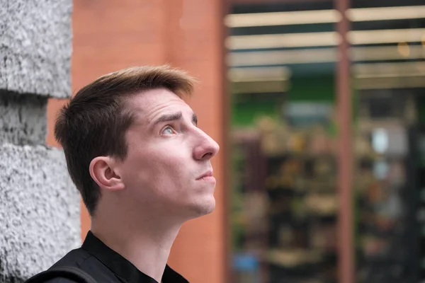 Portrait of a young handsome guy in a black shirt next to a brick wall autumn street photography