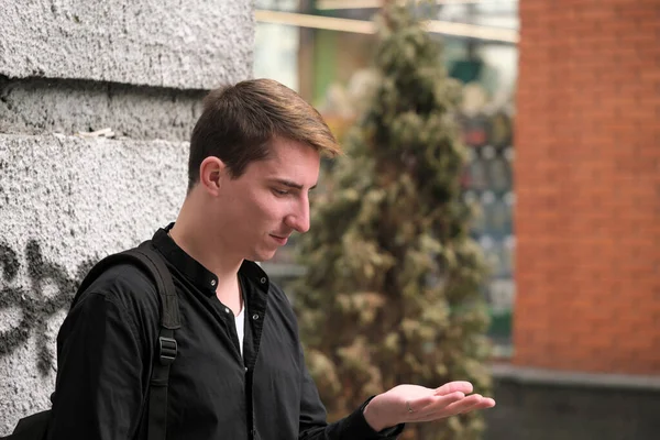 Portrait of a young handsome guy in a black shirt next to a brick wall autumn street photography