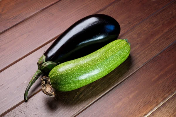 Fruits of green zucchini and blue eggplant on a textured wooden table close-up