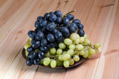 Olgun, beyaz ve siyah, yıkanmamış üzümler, cildinde doğal balmumu olan açık ahşap bir masa.