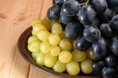 Olgun, beyaz ve siyah, yıkanmamış üzümler, cildinde doğal balmumu olan açık ahşap bir masa.