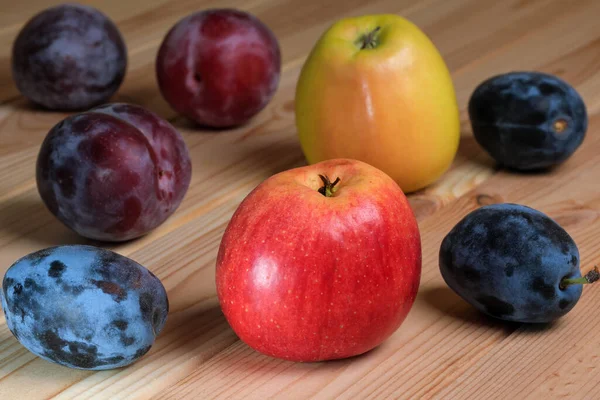 Sweet ripe apples and plums on a light wooden table close-up