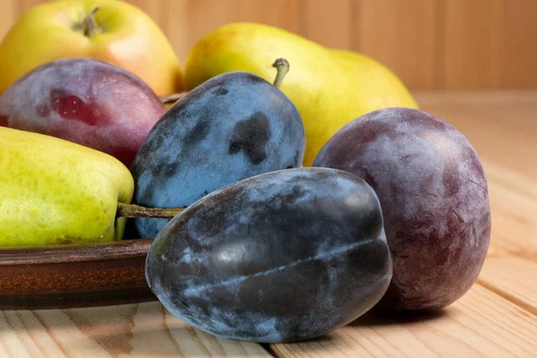Sweet ripe pears, apples and plums on a light wooden table close-up