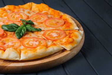 Gri ahşap arka planda pizza, yan görüş, yakın çekim. Peynirli, fesleğenli, domatesli, soslu, mozarellalı vejetaryen pizza. metin için yer.