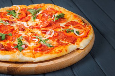 Gri ahşap arka planda pizza, yan görüş, yakın çekim. Peynirli, soslu, roka, biberli, biberli, biberli, soğanlı, sosisli, domatesli pizza. metin için yer.