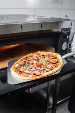 Pizzacı elektrikli fırından bitmiş pizzayı çıkarır. Pizzaiolo kürek kemiğinde pizza tutuyor..