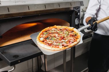 Pizzacı elektrikli fırından bitmiş pizzayı çıkarır. Pizzaiolo kürek kemiğinde pizza tutuyor..
