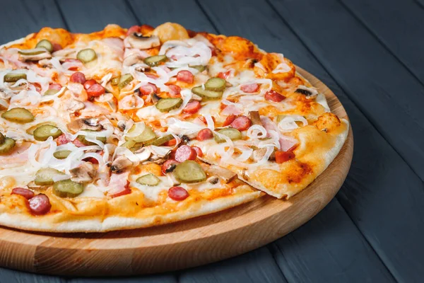 Gri ahşap arka planda pizza, yan görüş, yakın çekim. Peynirli pizza, salatalık turşusu, sos, soğan, mantar, pastırma, sosis. metin için yer.