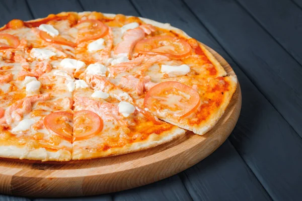 Gri ahşap arka planda pizza, yan görüş, yakın çekim. Pizza, sos, balık, mozzarella, krem peynir, domates, somon. metin için yer.