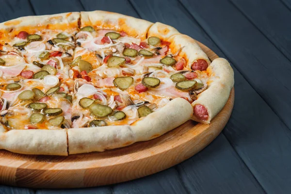 Gri ahşap arka planda pizza, yan görüş, yakın çekim. Peynirli pizza, salatalık turşusu, sos, soğan, mantar, pastırma, sosis. metin için yer.