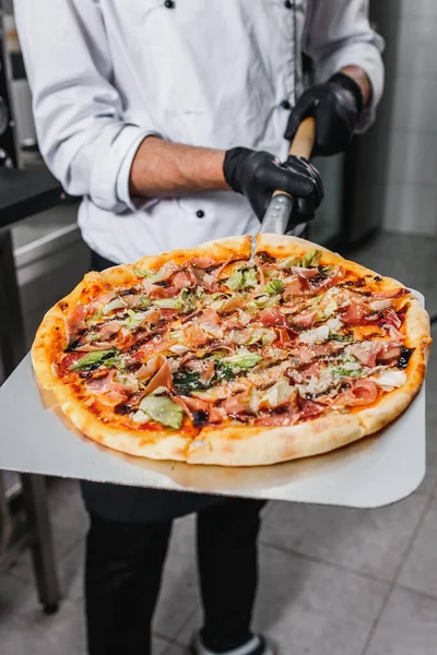 Pizzacı elektrikli fırından bitmiş pizzayı çıkarır. Pizzaiolo kürek kemiğinde pizza tutuyor..