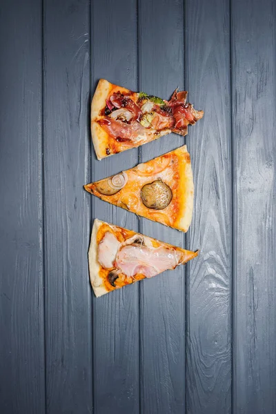 Tahta bir masanın üzerinde çeşitli pizzalar yatar. Yukarıdan bak. Birkaç dilim lezzetli ve iştah açıcı pizza..