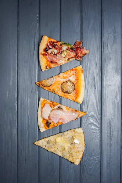 Tahta bir masanın üzerinde çeşitli pizzalar yatar. Yukarıdan bak. Birkaç dilim lezzetli ve iştah açıcı pizza..