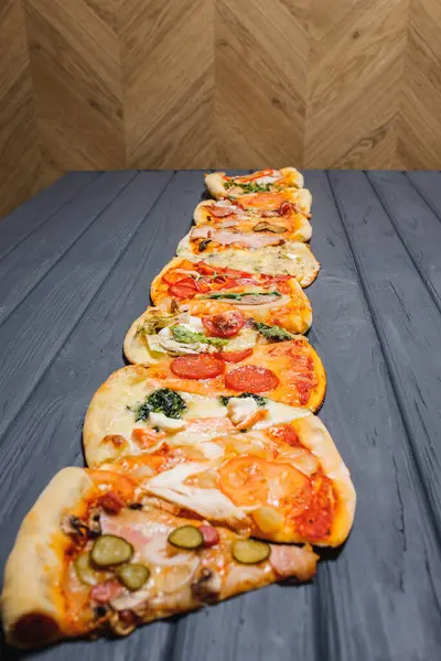 Tahta bir masanın üzerinde çeşitli pizzalar yatar. Yan görünüm.