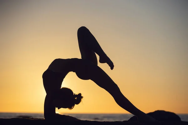 Frau übt Stretching bei Sonnenuntergang. Meer Hintergrund, Silhouette — Stockfoto