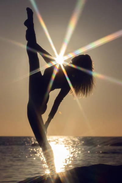 Gün batımında esneme alıştırması yapan kadın. deniz kenarı arkaplan, siluet — Stok fotoğraf