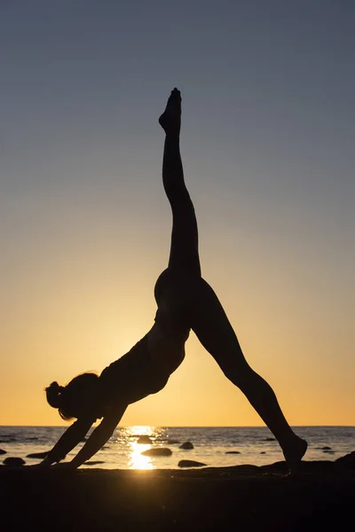 Kvinna tränar stretching vid solnedgången. havet bakgrund, silhuett — Stockfoto