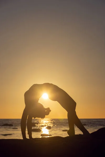 日没時にストレッチを練習する女性。海辺の背景シルエット — ストック写真