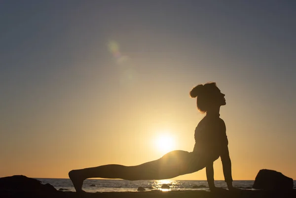 Frau übt Stretching bei Sonnenuntergang. Meer Hintergrund, Silhouette — Stockfoto