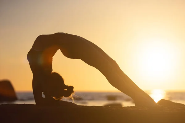 Kvinna tränar stretching vid solnedgången. havet bakgrund, silhuett — Stockfoto
