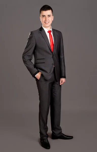 Young businessman standing on grey background — Stock Photo, Image