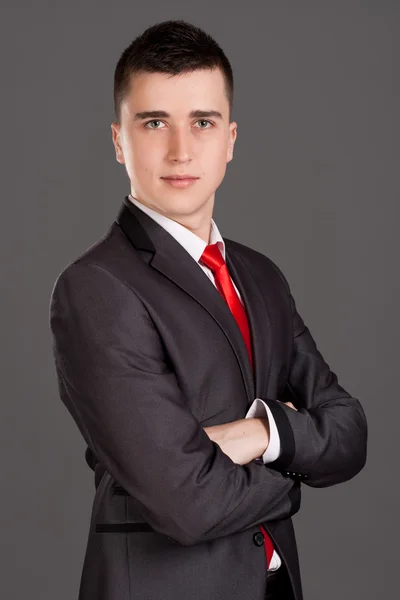 Young businessman standing on grey background — Stock Photo, Image